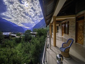 A balcony with a view of mountains, a wicker chair, and a metal railing. - New Brahma Guesthouse (Sosan)