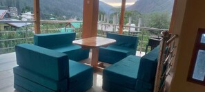 A balcony with blue cushioned seating and a small table, overlooking a mountainous landscape. - New Brahma Guesthouse (Sosan)