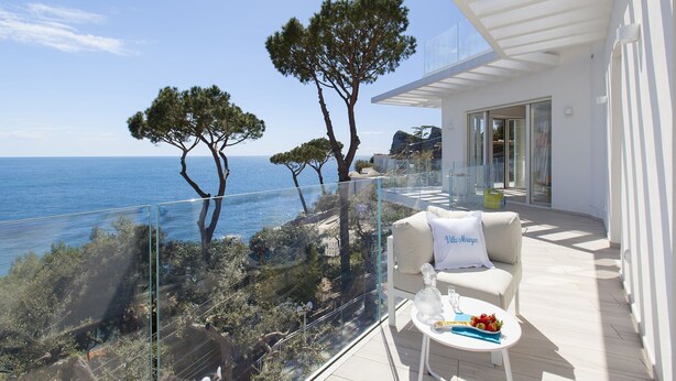 Un balcon moderne offrant une vue dégagée sur la mer, aménagé avec un canapé blanc et une petite table sur laquelle se trouvent une bouteille et des fruits.