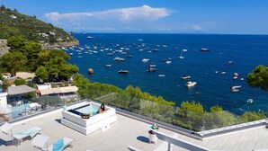 Un espace piscine aménagé sur le toit, avec des chaises longues et une balustrade en verre donnant sur une marina où sont amarrés de nombreux bateaux.