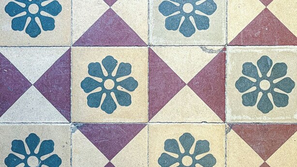 A tiled floor with a geometric pattern of triangles and squares, each featuring a central floral motif. - At Laura's House (Catania)