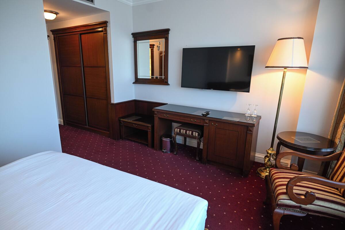 A hotel room with a bed, a desk, a chair, a TV, and a lamp.