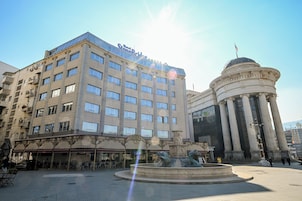 Un hotel con fachada moderna, un patio central con fuente y arquitectura clásica en los alrededores.