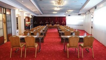 Un salón de conferencias con filas de mesas y sillas, piso de moqueta roja y un candelabro.