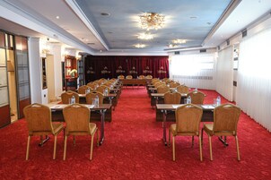 Un salón de conferencias con filas de mesas y sillas, piso de moqueta roja y un candelabro.