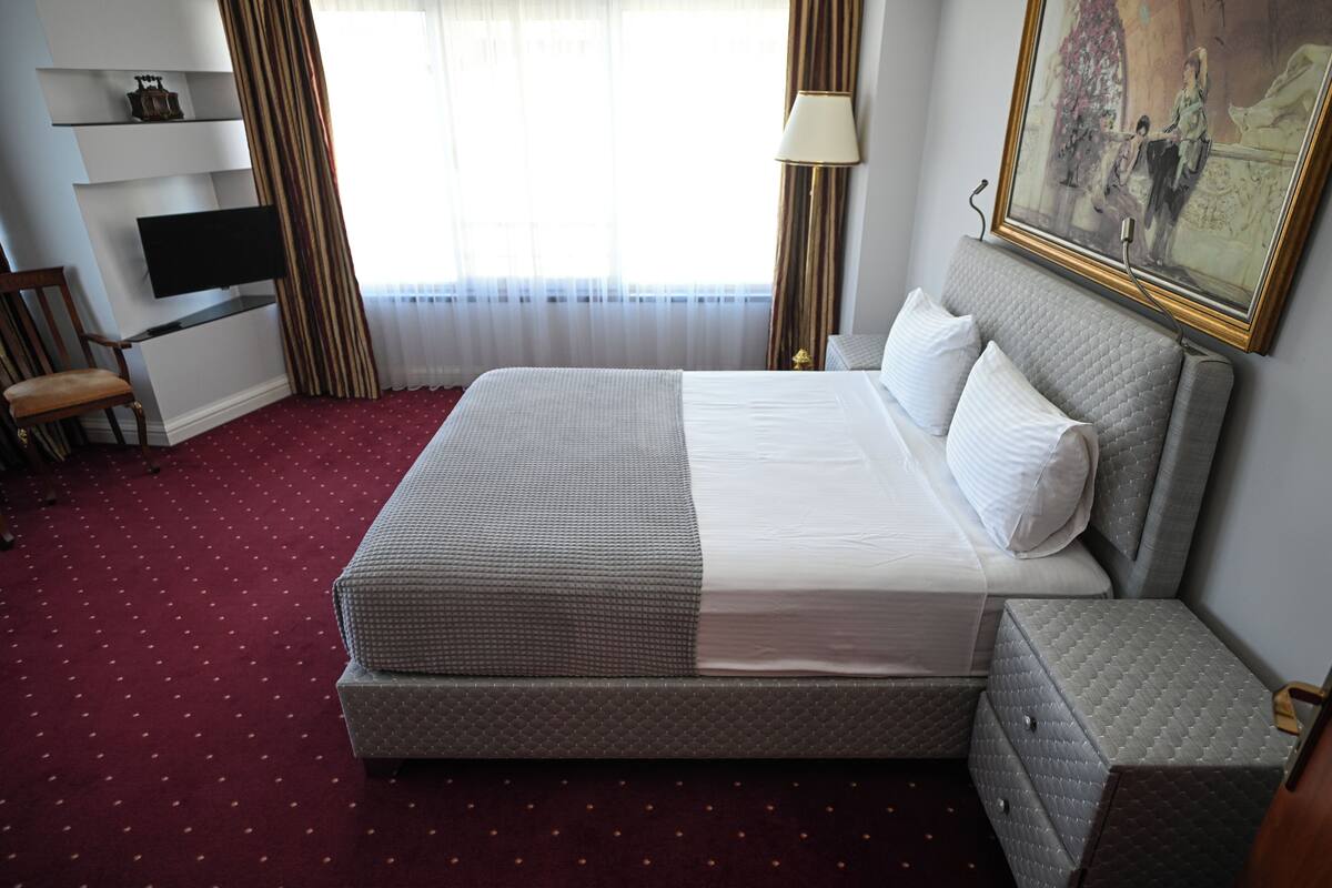 A neatly arranged hotel room with a large bed, a television, a chair, and a painting on the wall.