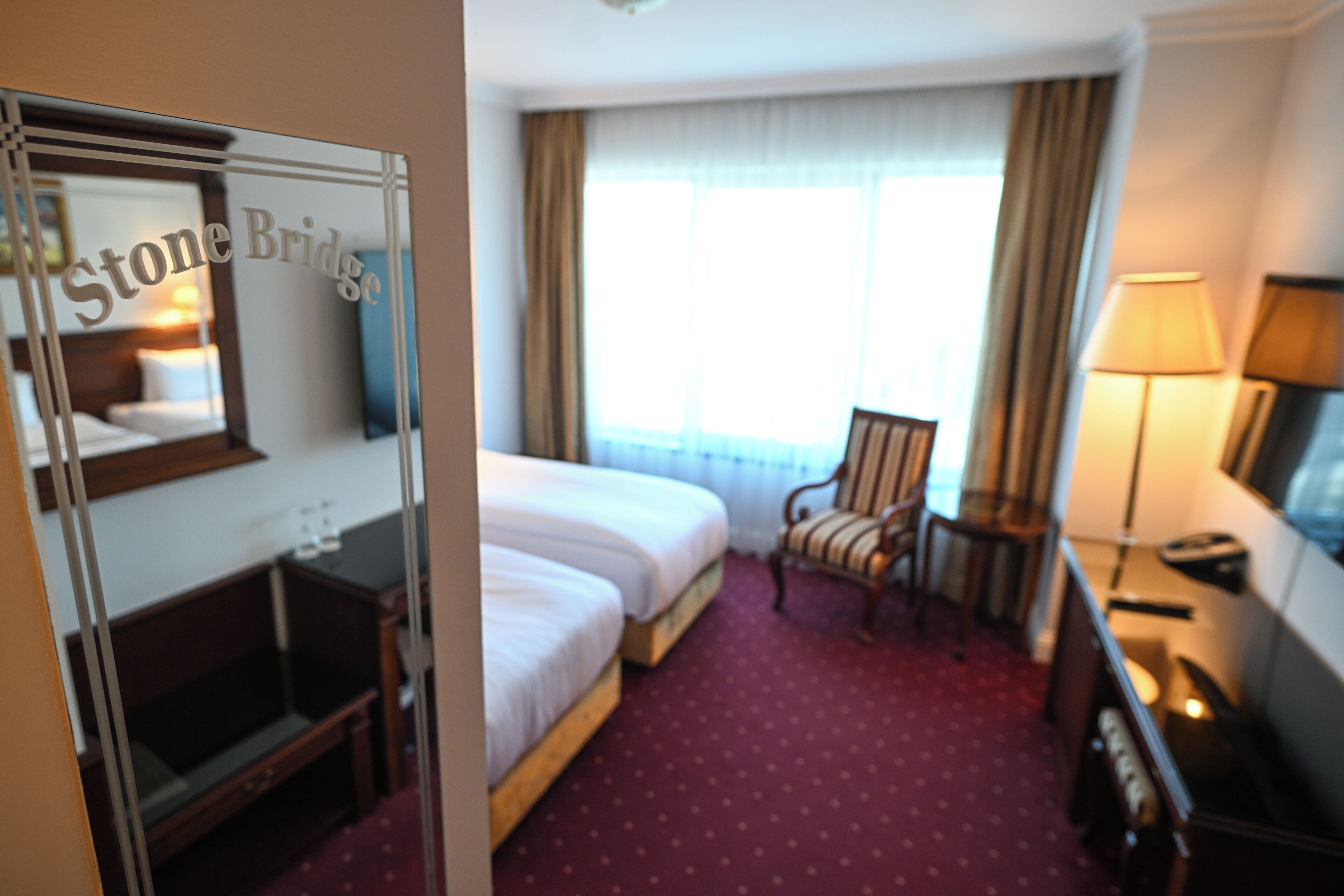 Una habitación de hotel con cama, una silla, un escritorio y una lámpara.