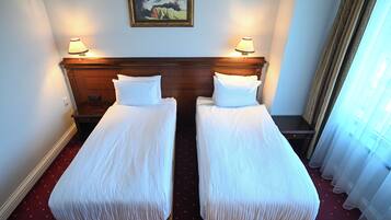 Una camera d'albergo con due letti singoli, una testiera in legno, un comodino, una lampada e un quadro appeso al muro.