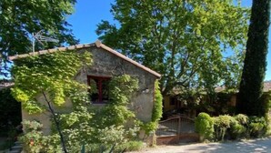 A rustic stone building with a red door, surrounded by lush greenery and trees. - Gite Grenache (Mondragon)