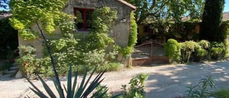 Un edificio de piedra rústico con una puerta roja, rodeado de abundante vegetación y árboles.