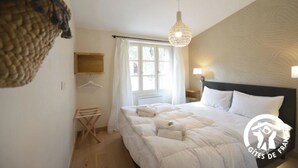 A bedroom with a large bed, a hanging light fixture, a window with curtains, and a wall-mounted TV. - Gite Grenache (Mondragon)