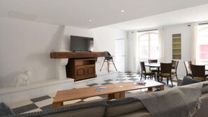 A modern living room with a sofa, a wooden coffee table, a TV mounted on a wooden cabinet, and a dining area with chairs and a table. - Gite Grenache (Mondragon)