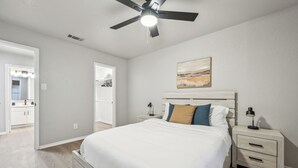 A bedroom with a bed, nightstands, a ceiling fan, and a painting on the wall.