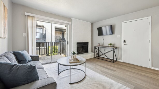 A living room with a sofa, a round coffee table, a fireplace, a TV mounted on the wall, and a balcony with a railing.