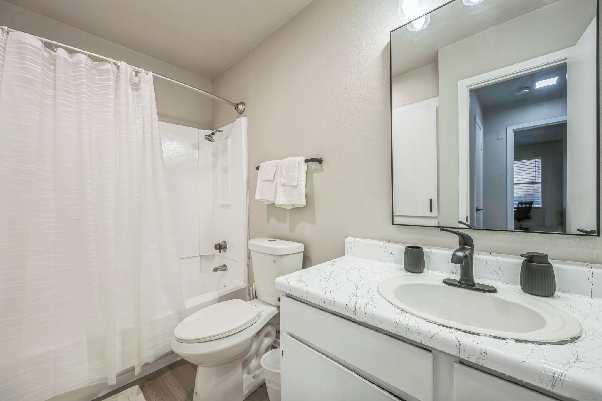 A modern bathroom with a white toilet, a shower with a curtain, a sink with a marble countertop, and a mirror above the sink.