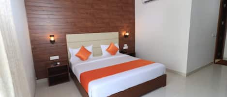A bedroom with a wooden headboard, a large bed with white and orange bedding, two bedside tables, and wall-mounted lights.