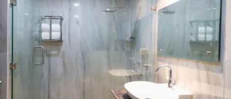 A modern bathroom with a glass shower enclosure, a marble floor, and a large mirror.