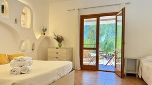 A bedroom with a bed, a nightstand, a dresser, a window with a view of greenery, and a sliding glass door leading to an outdoor area. - [Green Hotel] Rural hotel double rooms (Orosei)