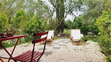 An outdoor seating area with a red table and chairs, surrounded by greenery and a stone pathway.