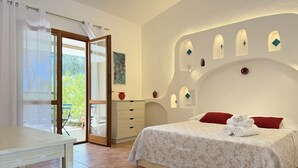 A bedroom with a bed, a table, a dresser, and a view of the outdoors. - [Green Hotel] Rural hotel double rooms (Orosei)
