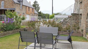 A patio with a table and chairs, surrounded by a garden with various plants and flowers. - Bright cottage in Swiss Normandy, pets allowed (Saint-Pierre-du-Regard)