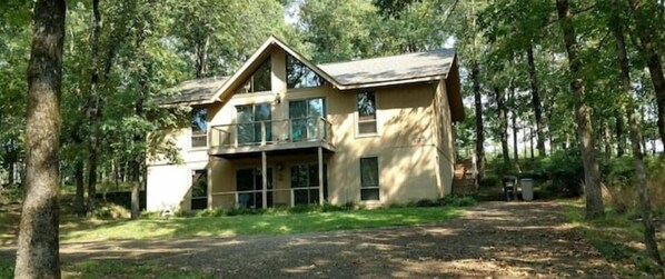 Enjoy a peaceful retreat in this serene two-story house surrounded by a wooded area, featuring a spacious balcony and a welcoming front entrance with a covered porch.