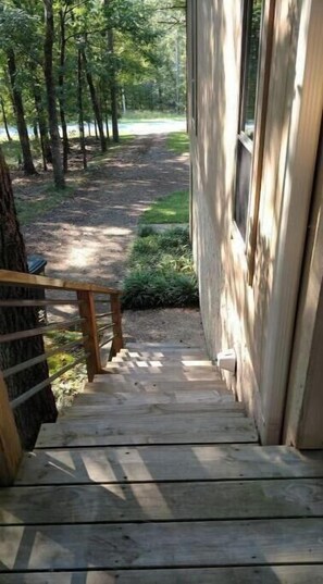 Stroll up the wooden staircase to a serene retreat surrounded by lush trees and a grassy area.
