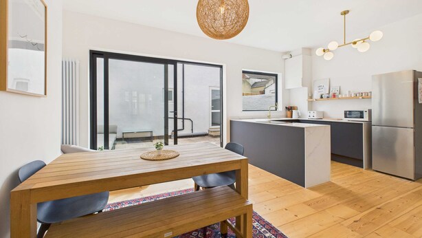 A modern kitchen with a central island, a dining area with a wooden table and chairs, and a large sliding glass door leading to a balcony.