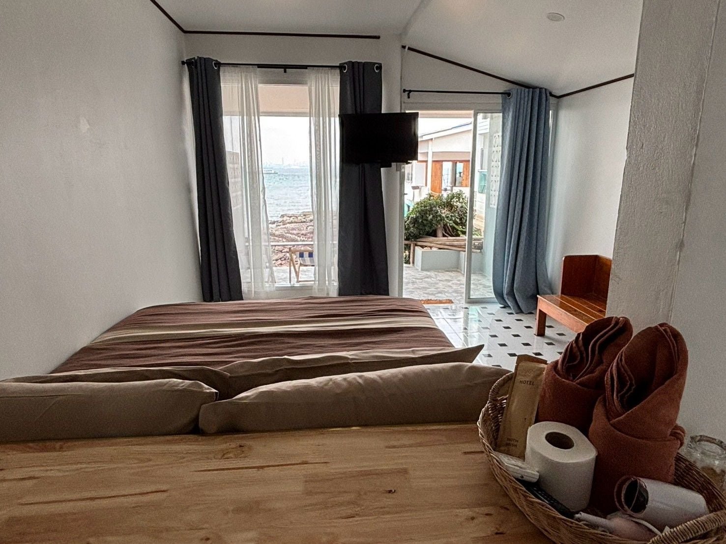 A hotel room with a bed, a TV, a balcony with a view, and a basket with towels.