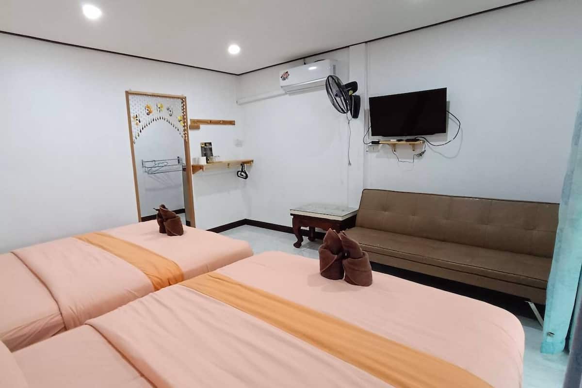 A hotel room with two beds, a sofa, a TV, an air conditioning unit, and a mirror.