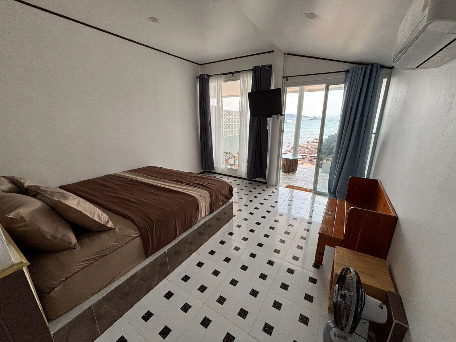 Una camera da letto con un letto, una scrivania, una sedia, una ventola e vista mare dalla finestra.