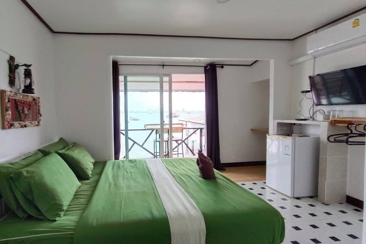 A room with a bed, a desk, a television, and a view of the sea.