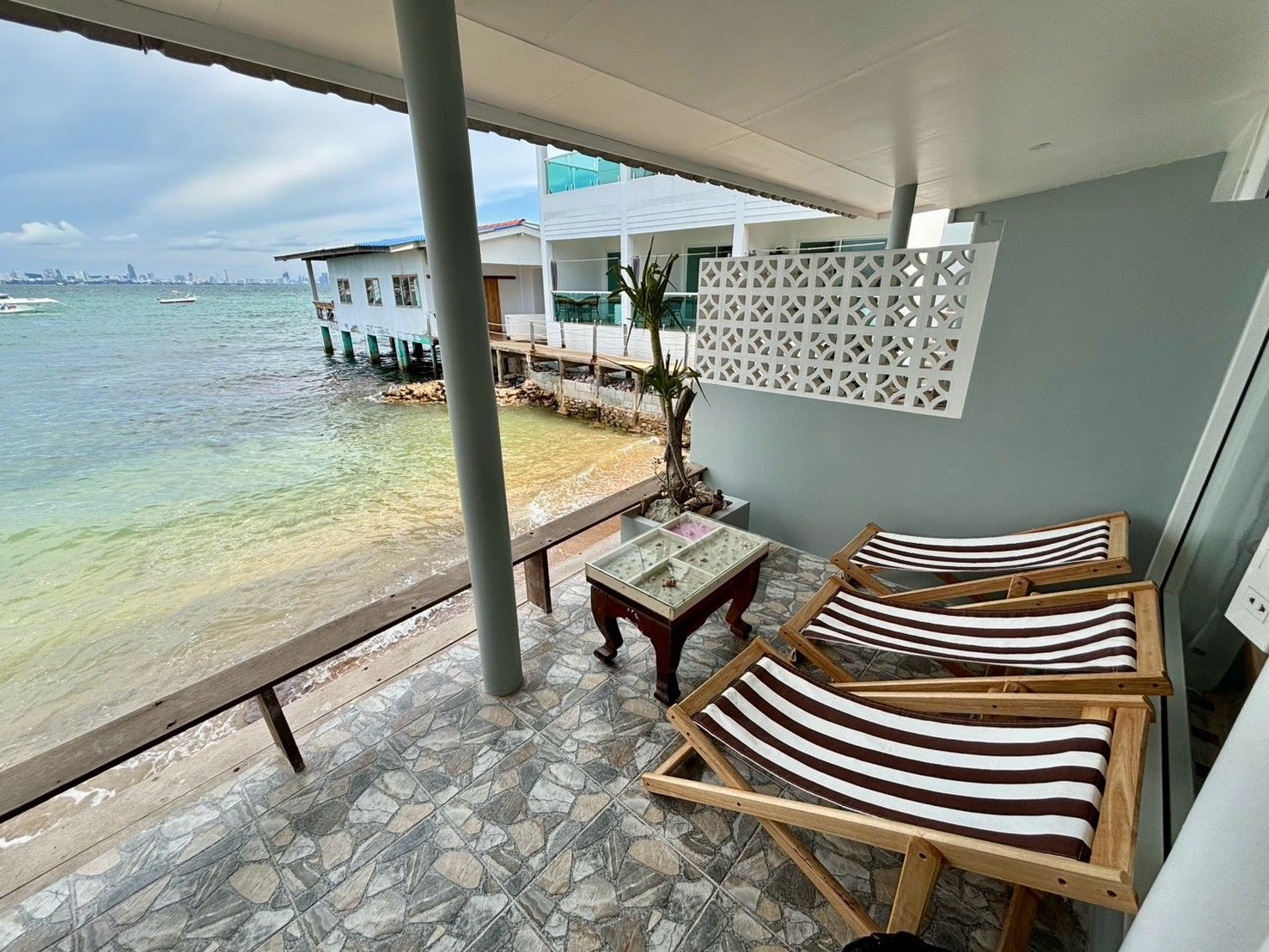 Een balkon met uitzicht op zee, een houten tafel en gestreepte lounge fauteuils.