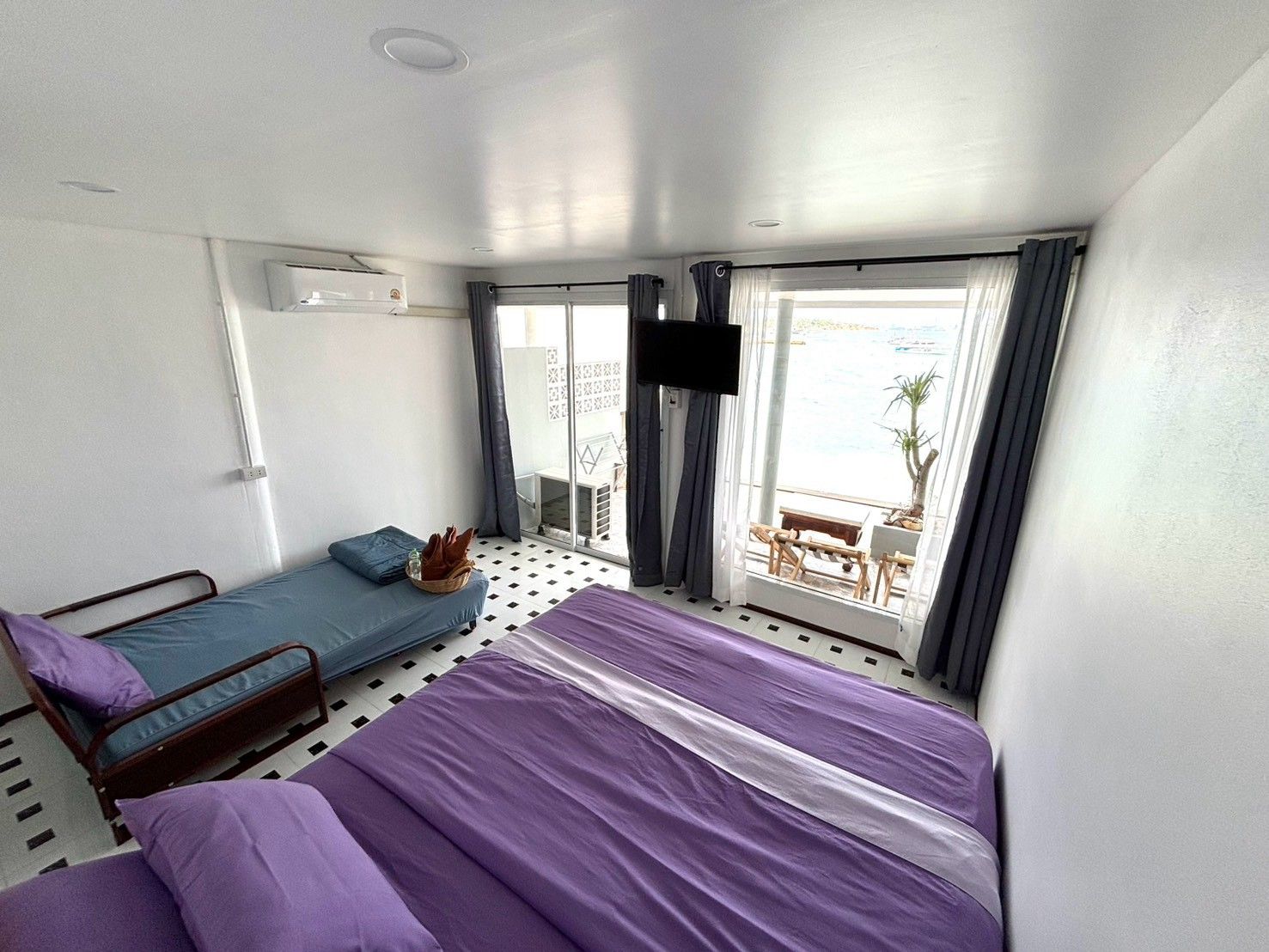 A compact hotel room with a bed, a small seating area, and a balcony with a view.
