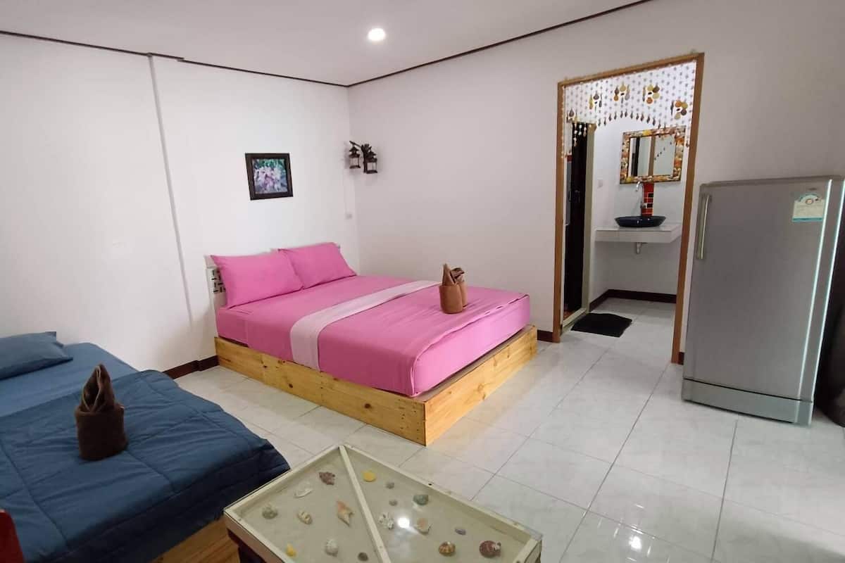 A bedroom with two beds, a small table, a refrigerator, and a bathroom with a sink and mirror.