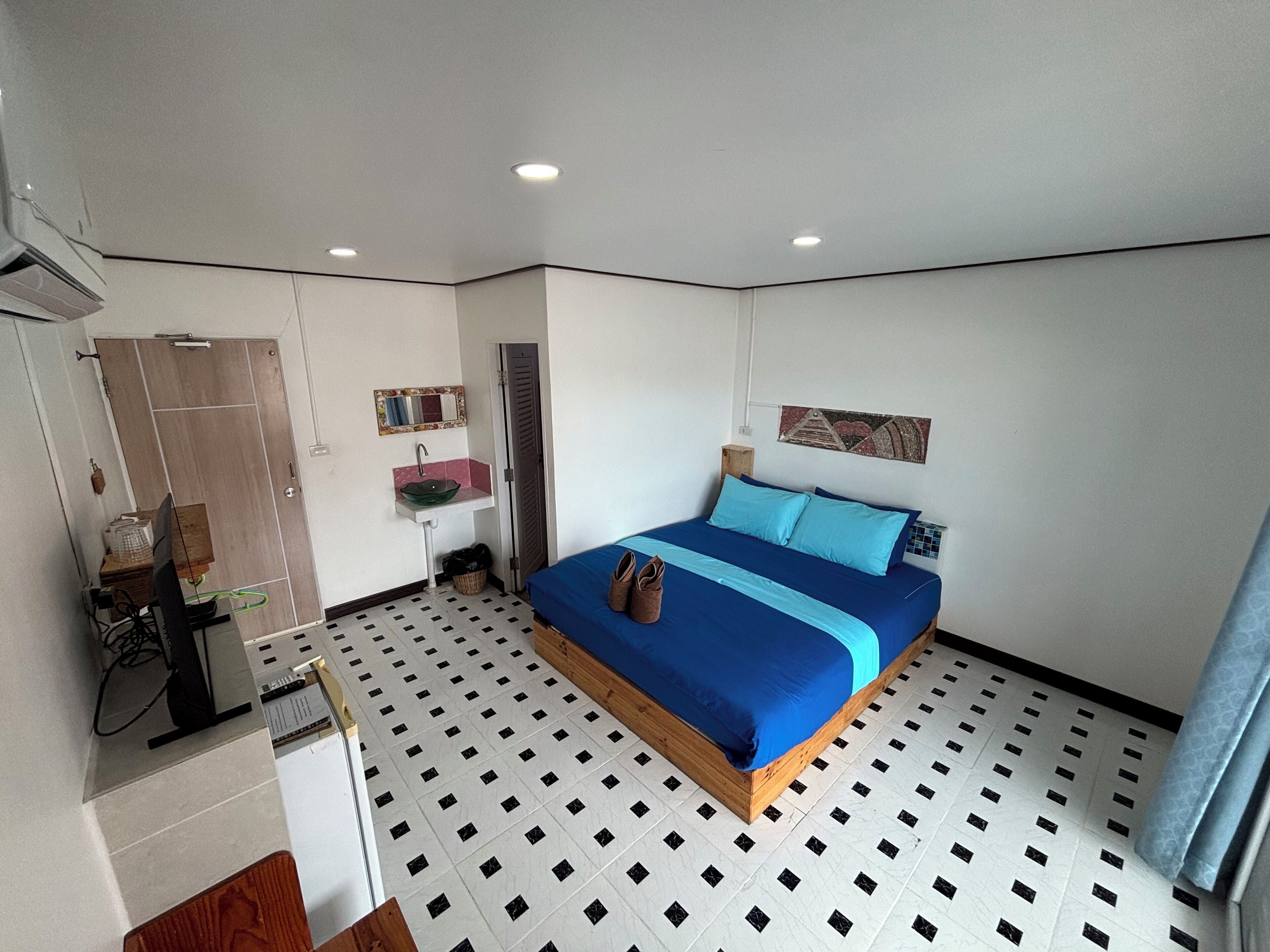 A bedroom with a bed, a sink, a mirror, and a door.