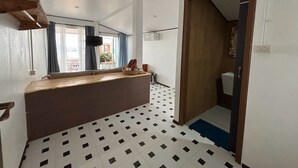 A hotel room with a kitchenette, a window with curtains, a tiled floor, and a wooden door. - Toonja kohlarn (Koh Lan)