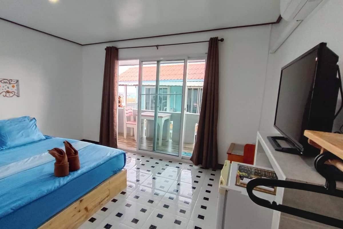 A bedroom with a bed, a TV, a desk, and a balcony with a view.
