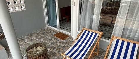 A balcony with stone tiles, a fire pit, and two striped beach chairs.