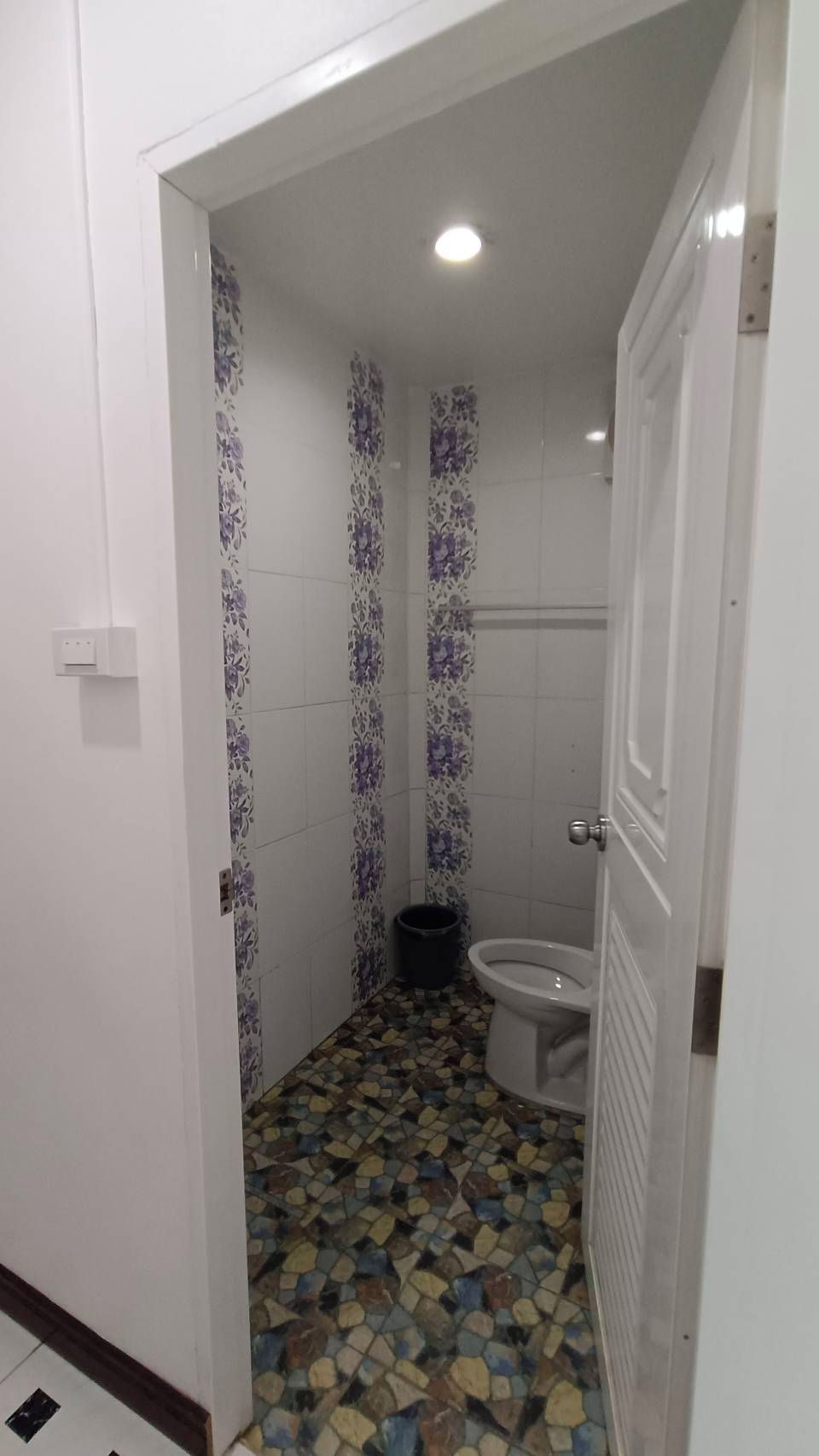 A bathroom with a tiled floor, a toilet, and a shower area.