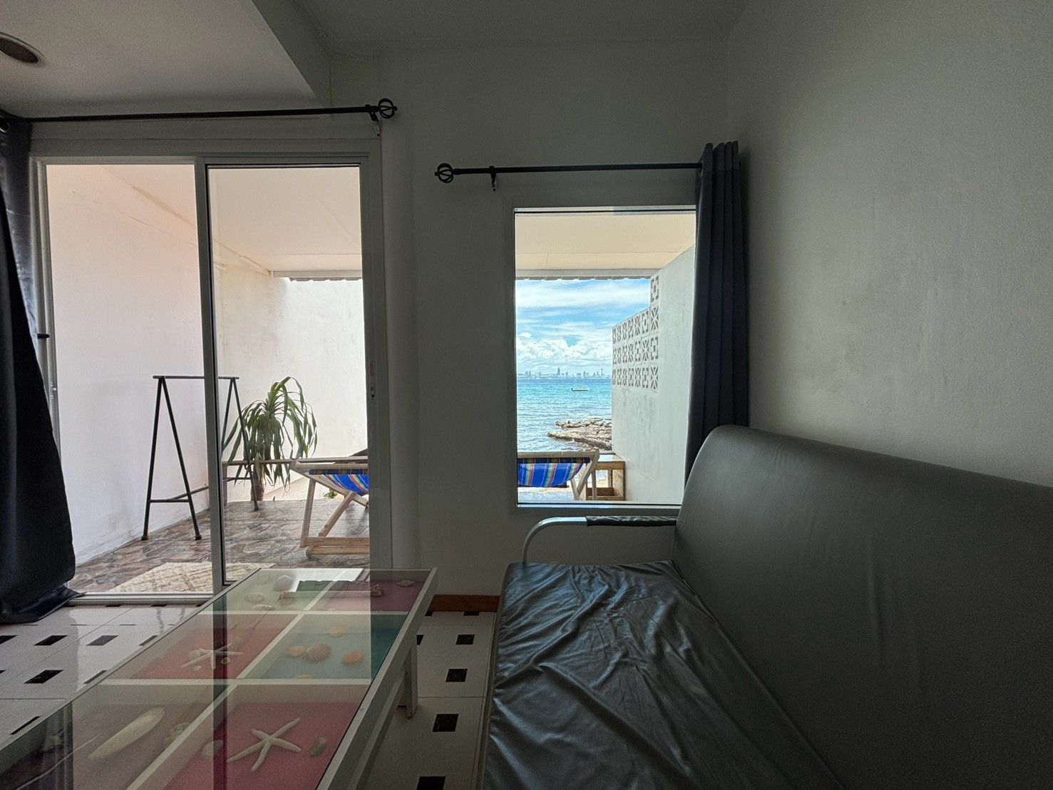Et værelse med en seng, et glasbord med pynteting, havudsigt og en balkon med stol og plante.