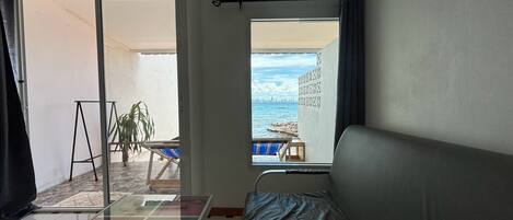 Et værelse med en seng, et glasbord med pynteting, havudsigt og en balkon med stol og plante.