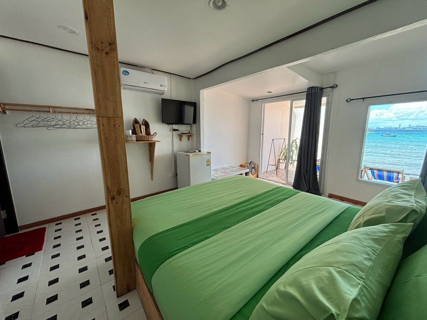 A room with a bed, a television, a window with a view of the sea, and a balcony with a chair.