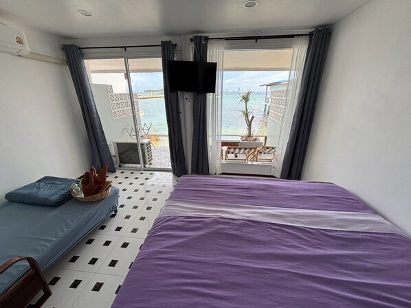 A hotel room with a bed, a seating area, a television, and a balcony with a view of the sea.