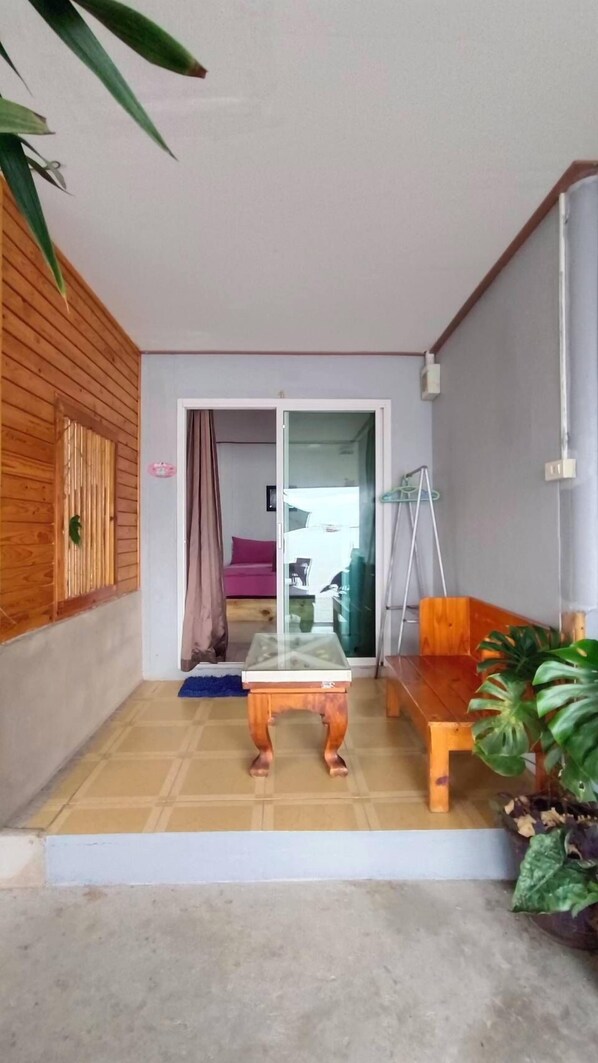 A room with a wooden floor, a glass door leading to another room, a wooden bench, and a potted plant.
