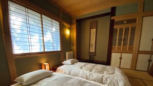 A traditional Japanese room with tatami flooring, two tatami mats, a shoji screen, a sliding door, and a hanging scroll.