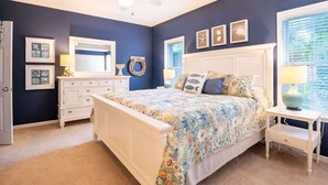 A bedroom with a large bed, a dresser, a vanity, and a ceiling fan.