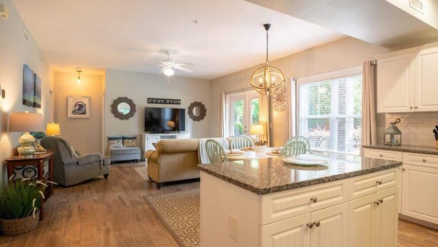 A spacious living room with a large island, a dining area, and a kitchen with white cabinets and granite countertops.
