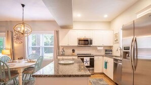 A modern kitchen with white cabinets, stainless steel appliances, and a granite countertop island.