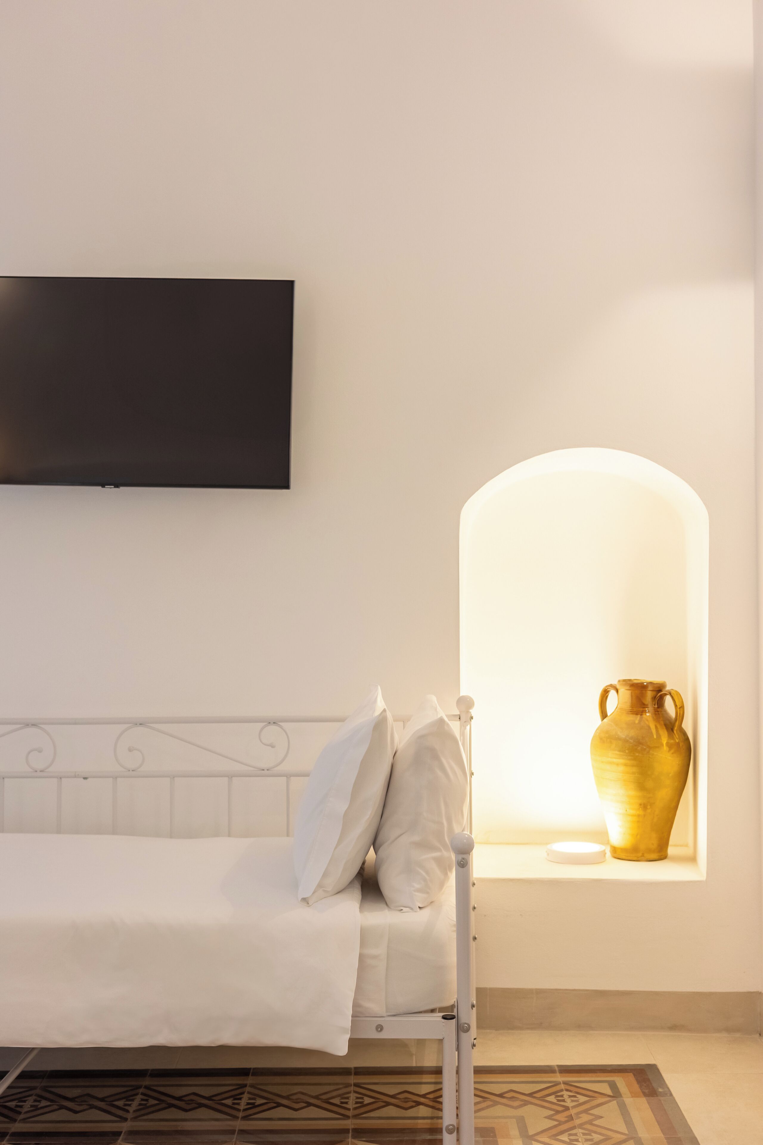 A bed with a white headboard, a flat-screen TV mounted above it, and a window with a decorative arch.